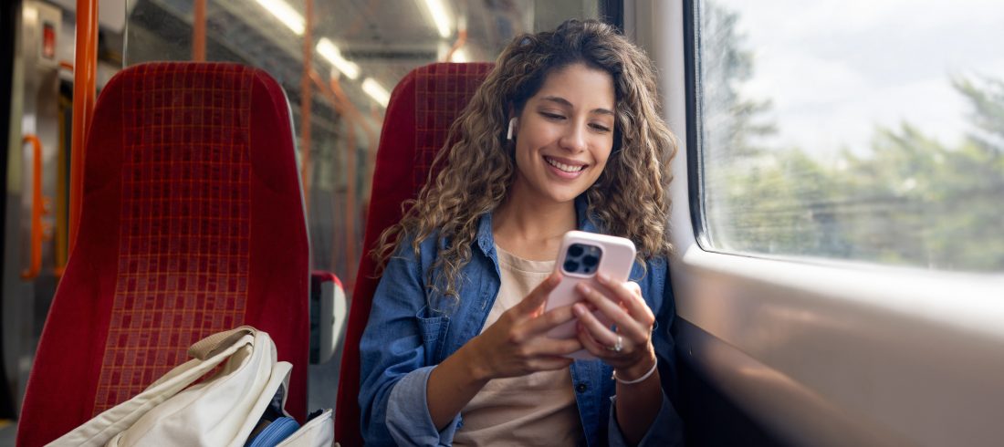 Happy woman commuting on a train and checking her cell phone